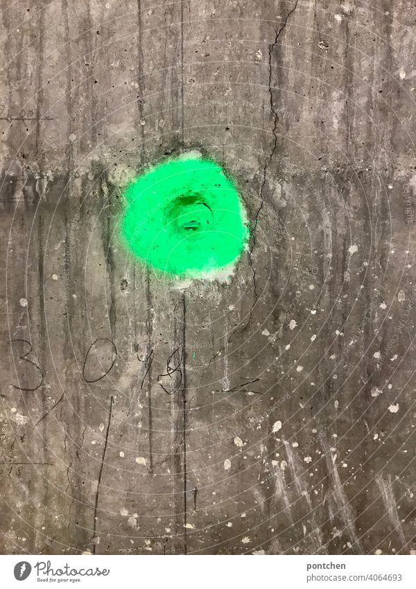 ein grüner punkt auf einer mauer aus beton. markierung neon farbe baustelle bauarbeiten