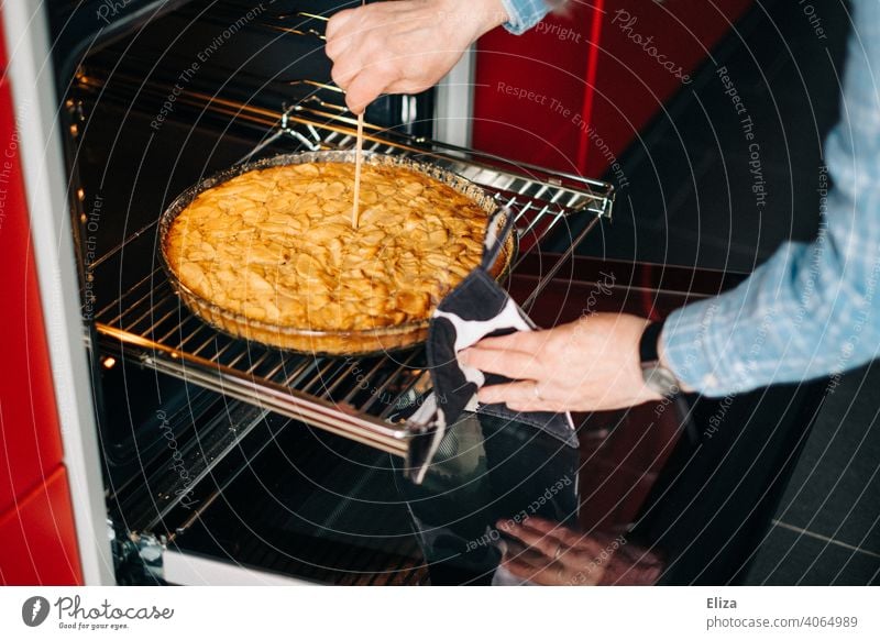 Eine Frau prüft mit einem Holzspieß ob der Apfelkuchen schon fertig gebacken ist prüfen Ofen Holzstäbchen Kuchen Küche süß Backwaren Teigwaren Apfeltarte