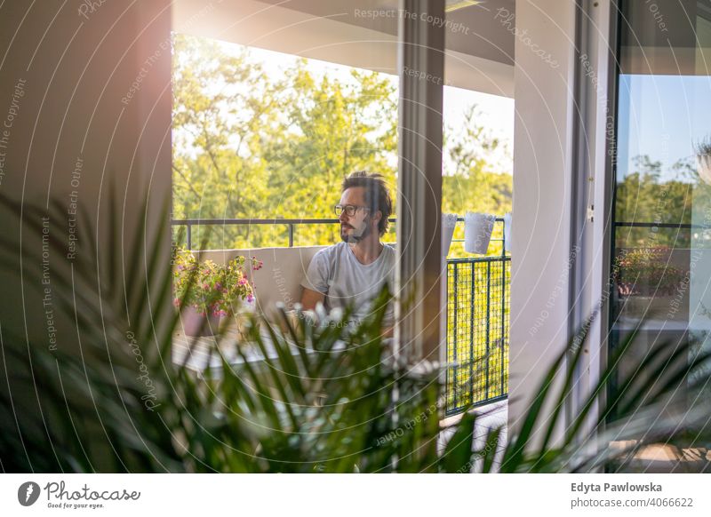 Mann trinkt Kaffee auf dem Balkon seiner Wohnung Frischluft ruhen Quarantäne Topfpflanze zu Hause bleiben Brille Sperrung einfaches Leben Terrasse