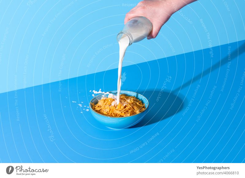 Gießen von Milch in einer Müslischale auf einem blauen Hintergrund. Cornflakes und Milch. abstrakt Getränk Flasche Schalen & Schüsseln Frühstück hell Zerealien