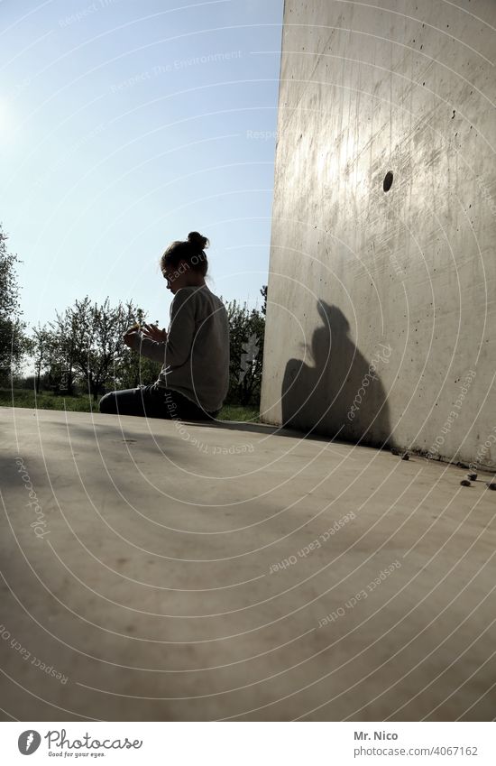 alleinsein teenager Jugendliche Mädchen Haare & Frisuren Dutt sitzen Sonne Schatten Beton Betonwand Betonboden Himmel Schönes Wetter Wand Perspektive Eingang