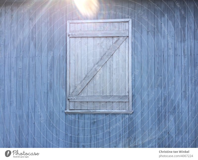 Blaue Holzfassade mit grauem, geschlossenen Fensterladen aus Holz. Reflexion durch einfallendes Sonnenlicht am oberen Bildrand zu Fassade Wand Gebäude