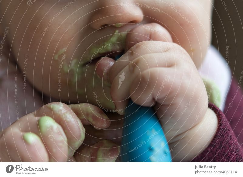 Nahaufnahme von Baby Fütterung selbst einen grünen Smoothie mit Löffel; chaotisch Baby geführt Entwöhnung babygeführte Entwöhnung Erstes Essen Babynahrung