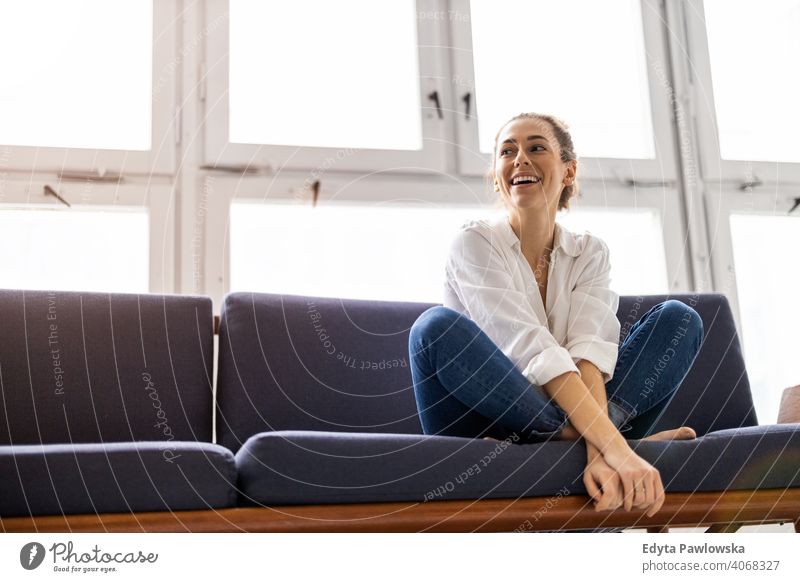 Junge Frau entspannt auf Sofa Sitzen Liege aussruhen entspannend bequem Pause Barfuß Lotos Yoga Meditation Jahrtausende Schüler Hipster im Innenbereich Loft