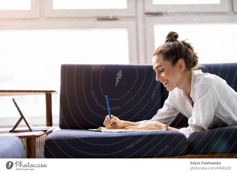 Junge Frau macht Hausaufgaben auf dem Sofa Sitzen Liege aussruhen entspannend bequem Jahrtausende Schüler Hipster im Innenbereich Loft Fenster natürlich Mädchen