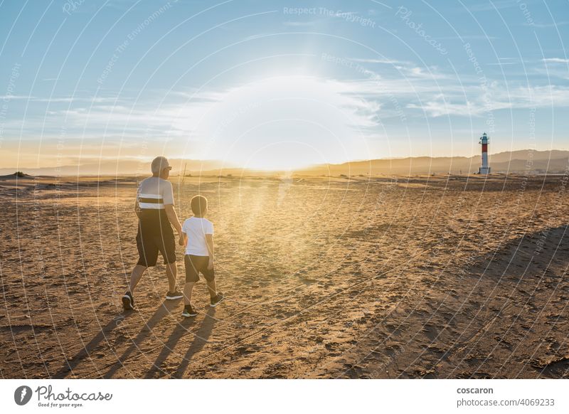 Großvater und Enkel umarmen sich an einem Strand mit einem Leuchtturm im Hintergrund Rücken Junge Kind Kindheit Kinder Küste Papa Tag älter Familie Fangar