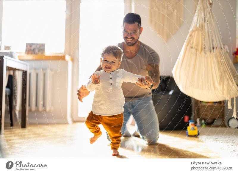 Kleiner Junge lernt laufen mit seinem Vater neben ihm zu Hause alleinerziehend alleinerziehender Vater Vatertag Vaterschaft zu Hause bleiben Dad