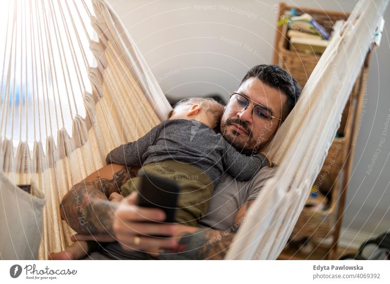 Mann überprüft sein Telefon, während sein kleiner Babysohn schläft alleinerziehend alleinerziehender Vater Vatertag Vaterschaft zu Hause bleiben Dad