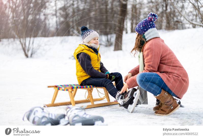 Mutter hilft Sohn beim Anziehen seiner Schlittschuhe Tochter Saison Zusammensein gefroren heiter Spaß Kind Menschen Park Feiertag Wald Kindheit Frau Mädchen