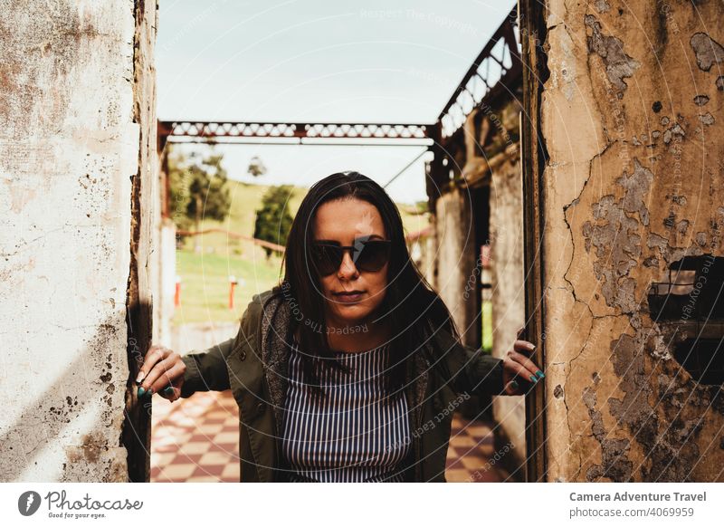 Lässig gekleidete Frau in der Mitte eines zerstörten Türrahmens, Nahaufnahme Outfit im Freien reisen Urlaub Ruinen lässig alt Struktur Mosaik Sonnenbrille Jacke