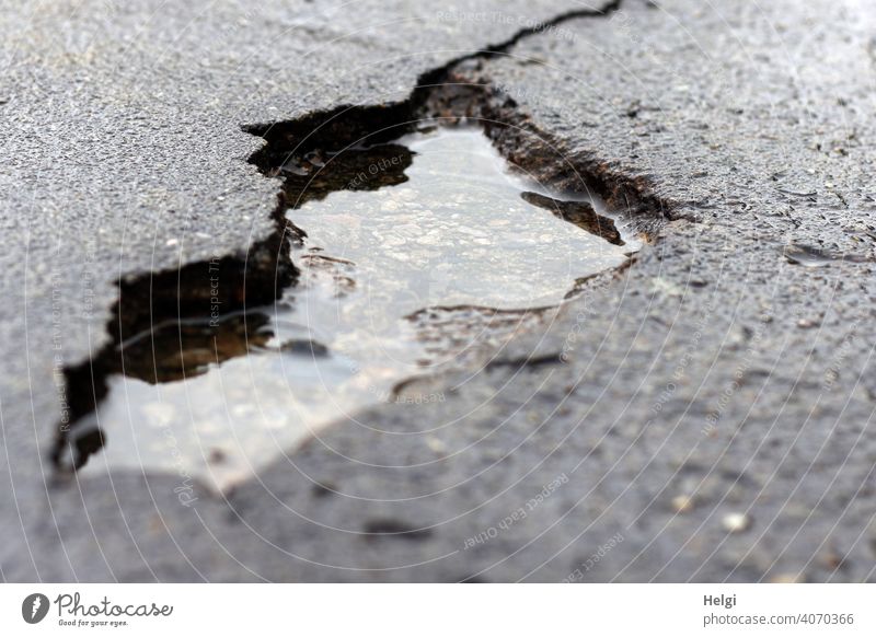großes Loch in der Teerdecke der Straße, gefüllt mit Regenwasser Straßenschaden kaputt beschädigt Wasser Pfütze Unfallgefahr Gefahr Schaden Menschenleer