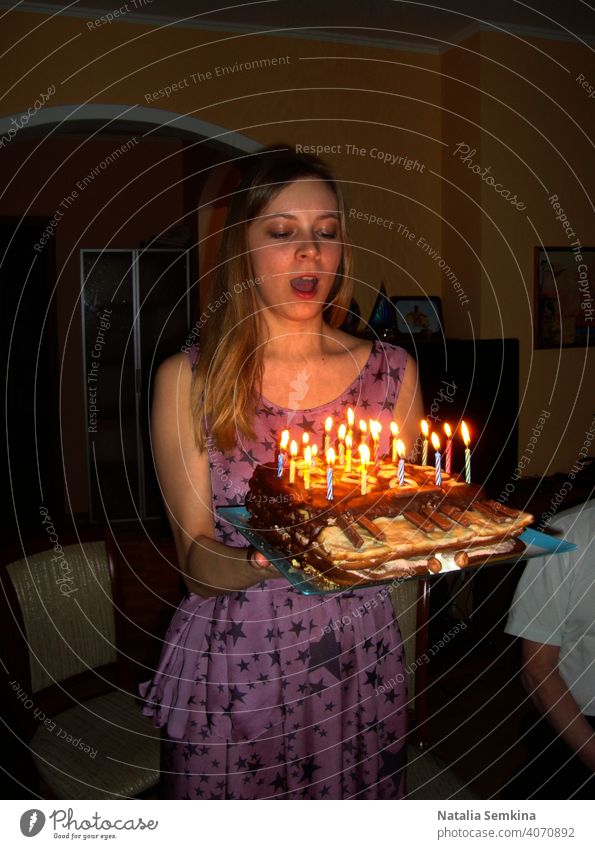 Junges Mädchen in lila Kleid hält handgemachte festlichen Kuchen in Klavierform mit brennenden Kerzen in ihren Händen in dunklen Raum. Geburtstagsfeier zu Hause. Vertikale Ausrichtung.