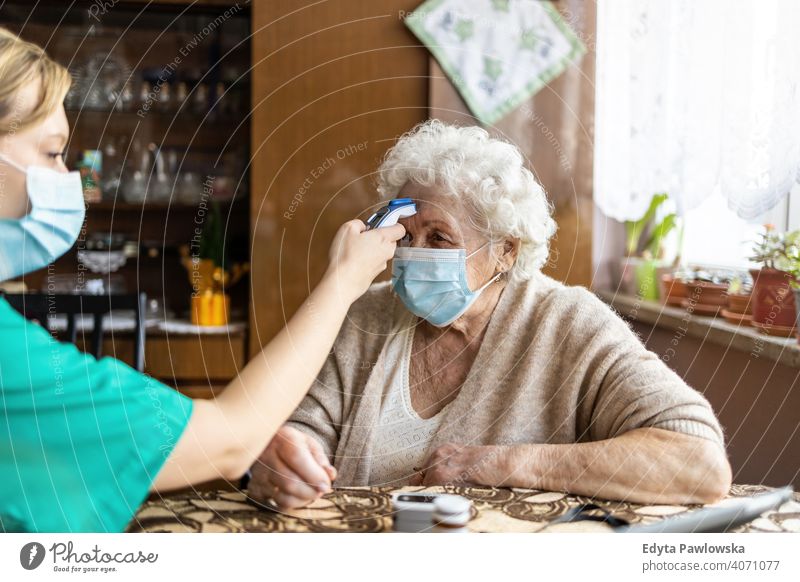 Krankenschwester prüft die Temperatur einer älteren Frau beim Hausbesuch Coronavirus Gesichtsmaske echte Menschen COVID Senior Krankenpfleger besuchen offen
