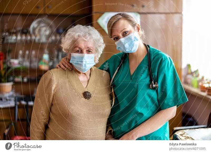 Ältere Frau wird während des Einschlusses von einer Pflegefachkraft besucht Coronavirus Gesichtsmaske echte Menschen COVID Senior Krankenpfleger älter besuchen