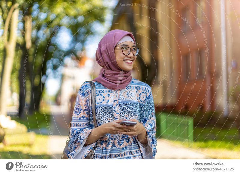 Lächelnde junge muslimische Frau mit Handy im Freien Hijab Kopftuch Islam arabisch Sommer Mädchen Menschen junger Erwachsener Lifestyle aktiv tausendjährig