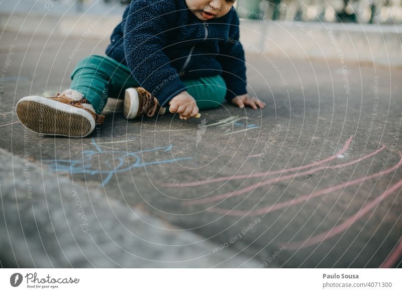 Kind zeichnet mit farbiger Kreide auf dem Boden Kaukasier 1-3 Jahre authentisch Kreidezeichnung Kindheit Spielen Farbfoto Strassenmalerei Kunst malen zeichnen