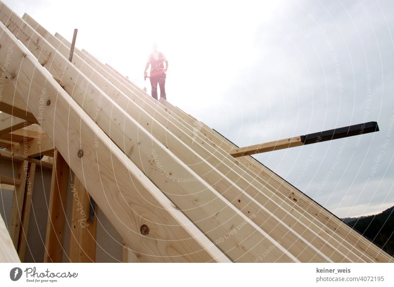 Ein Zimmermann auf einem Dachstuhl stehend im Gegenlicht der Sonne wie der letzte Handwerker der Nation bauen Bauhandwerk baukosten anonym Bauwirtschaft Mann