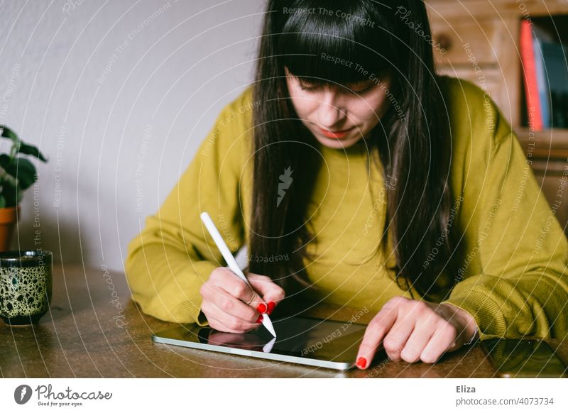 Eine Frau sitzt am Tisch und zeichnet oder schreibt etwas auf einem Tablet malen schreiben zeichnen Stift ipad Apple Pen Kreativität digital Grafikerin