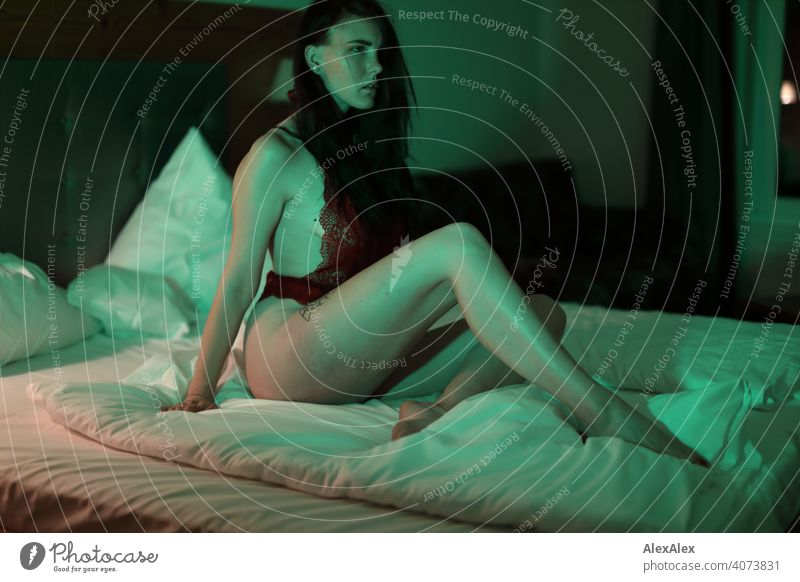 Junge Frau mit roter Lingerie sitzt im Hotelbett und ist in grünes Licht getaucht junge Frau Bett Hotelzimmer lieben schlank schön erotisch sinnlich sportlich