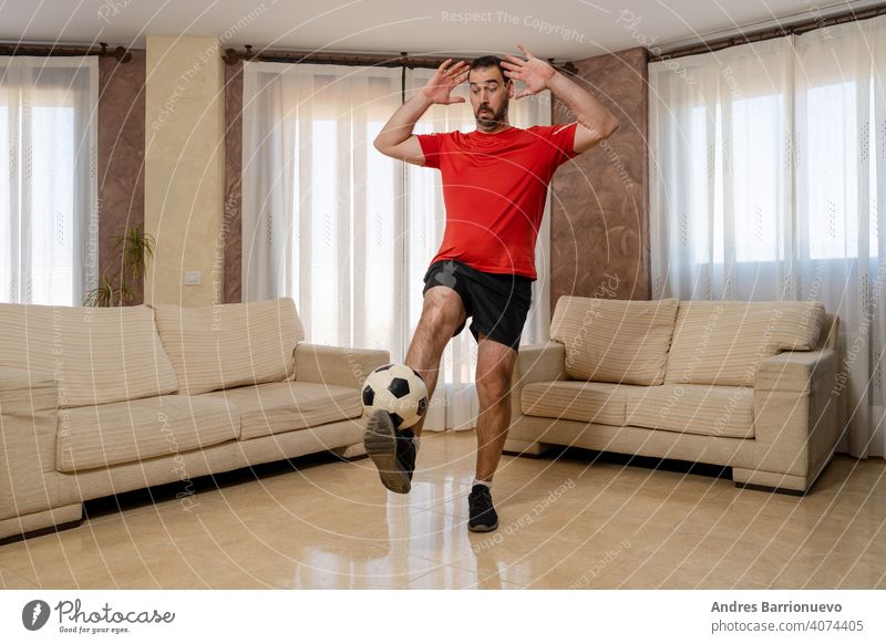 Bärtiger Mann in fitter Form, gekleidet in schwarzer und roter Sportkleidung, der einen Fußball mit dem Fuß kontrolliert Verehrer Erwachsener heimwärts