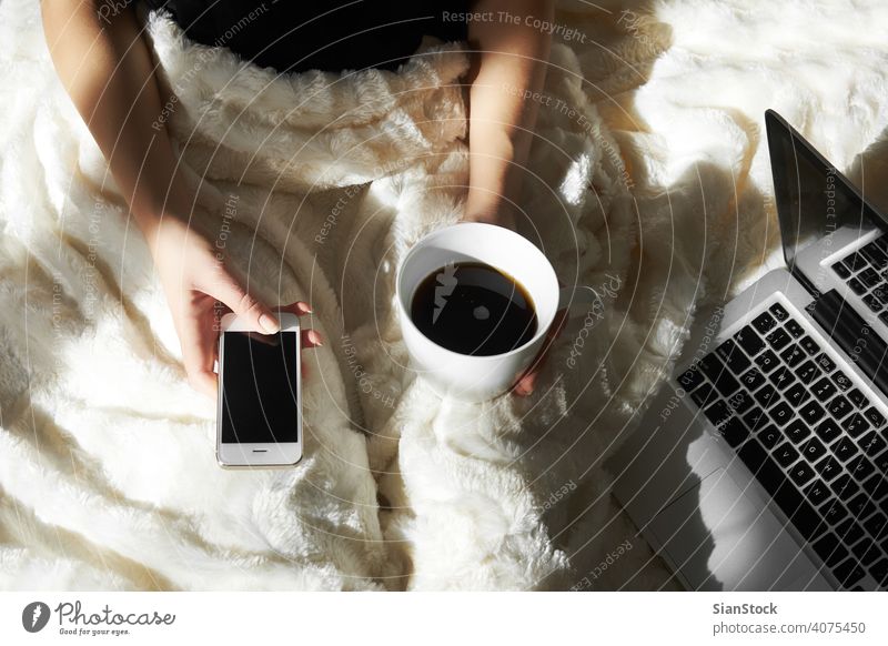 Junge Frau trinkt Kaffee zu Hause in ihrem Bett und überprüft ihr Smartphone Laptop Tasse Computer Tippen jung Bildung Lügen Mädchen Hand heimwärts Person