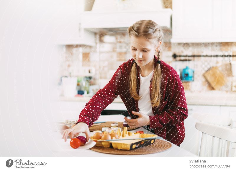 Kleine Blondine zu Hause in der Küche malt Ostereier in verschiedenen Farben für Ostern Frühling Kind Feiertag Vorbereitung Schwestern Bruder Ei hell Familie
