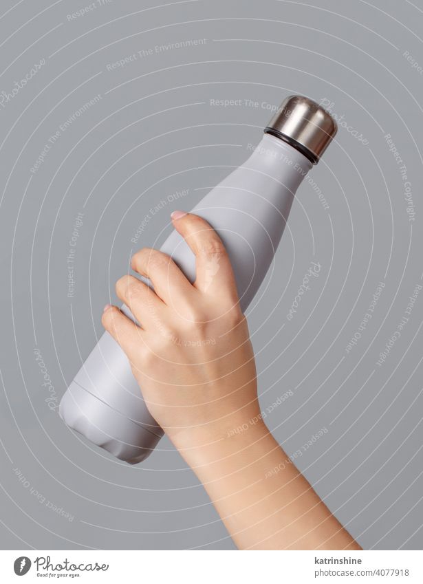 Hand mit grauer wiederverwendbarer Isolierflasche auf grauem Hintergrund Flasche Attrappe isoliert ökologisch Wasser Stahl Thermo Leichtmetall blanko
