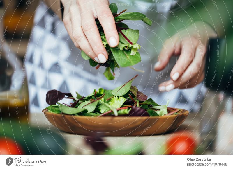 Frau legt eine Salatmischung auf einen Holzteller. Salatbeilage Hand setzen Mittelteil Selektiver Fokus abschließen Teller Herstellung hölzern Tomate Rucola