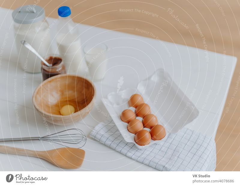 Kochen Zutaten auf dem Küchentisch. Blick von oben auf Eier, Milch und Mehl, Schneebesen und Holzspatel in der Nähe. Utensilien und frische Produkte Rührbesen