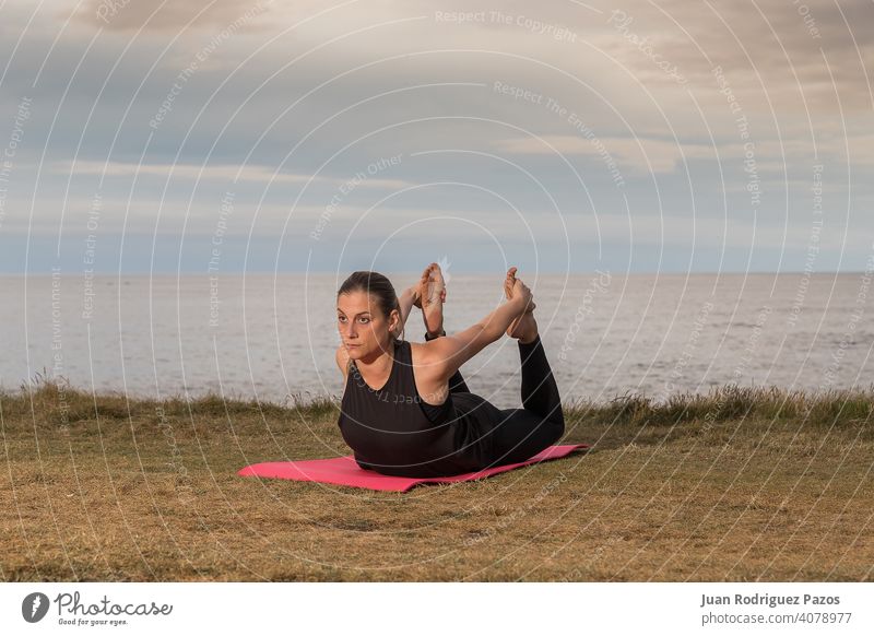 Frau in schwarzer Sportkleidung beim Training im Freien mit dem Meer im Hintergrund. Pilates Yoga Übung Gesundheit Lifestyle MEER Unterlage strecken Fitness