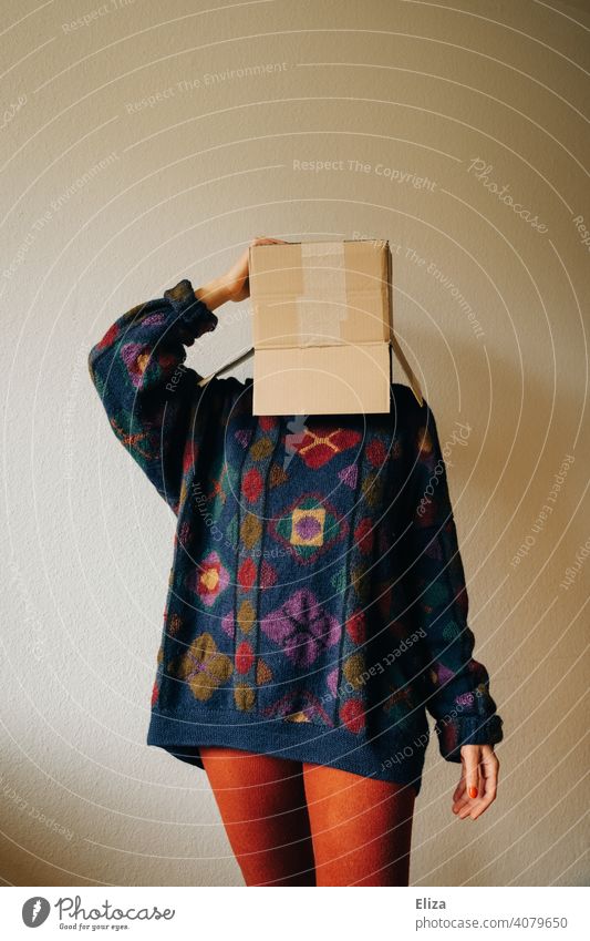 Frau in bunter Kleidung mit einem Karton auf dem Kopf Kiste verschicken bestellen anonym verstecken genervt Paket Schachtel Verpackung Pappkarton Pullover dsgvo