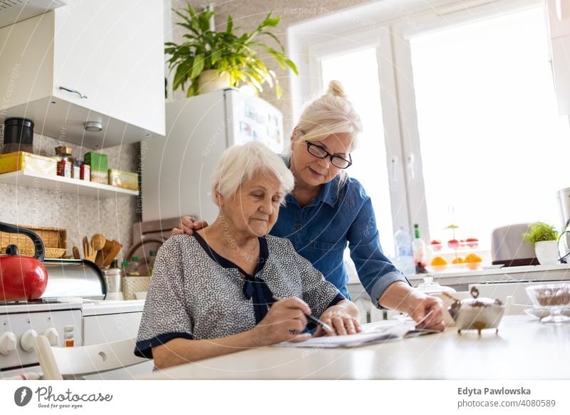 Ältere Frau hilft ältere Mutter mit Papierkram Wille Schriftstück Diskussion über schreibend Finanzen Geld Verwirrung lesen Küche heimisch Unterstützung