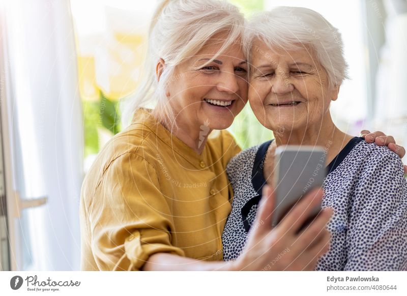 Ältere Frau und ihre erwachsene Tochter nutzen gemeinsam ein Smartphone Lächeln Glück genießend Positivität Vitalität Freude Selbstvertrauen Menschen Senior