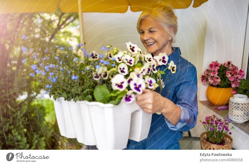 Seniorin, die sich um ihre Pflanzen auf dem Balkon kümmert Lächeln Glück genießend Positivität Vitalität Freude Selbstvertrauen Menschen Frau reif lässig