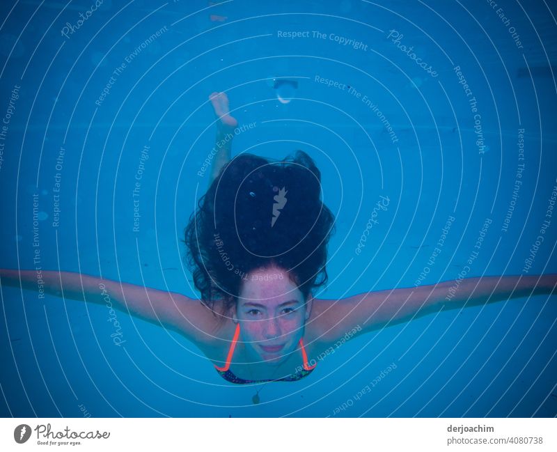 Ein junges Mädchen schwimmt , im  blauen Wasser ,unter mit weit ausgebreiteten Armen und die dunklen Haare schweben über Ihr. Schwimmende flügel Natur Sommer