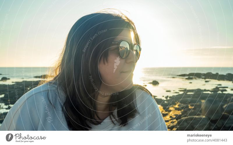 Seitliche Nahaufnahme einer kaukasischen Frau mit Sonnenbrille während eines Sonnenuntergangs am Meer abschließen Kaukasier Nur eine Frau Lifestyle Farbbild