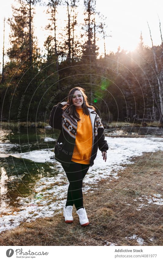 Fröhliche junge Frau am Teich im Wald Glück Wanderer heiter reisend freudig Tourismus Wiese Schnee Wetter Freizeit Fußweg Bäume Sonnenlicht Lifestyle Lächeln
