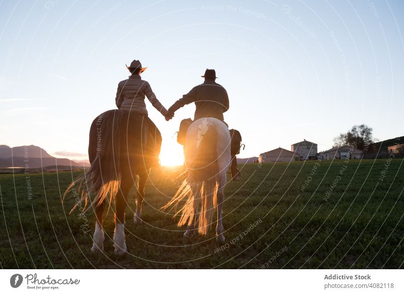 Menschen auf Pferden halten Hände Reiten Händchenhalten Ranch Sonnenuntergang Himmel Abend Mann Frau gestikulieren Sport Pferderücken Reiterin Lifestyle