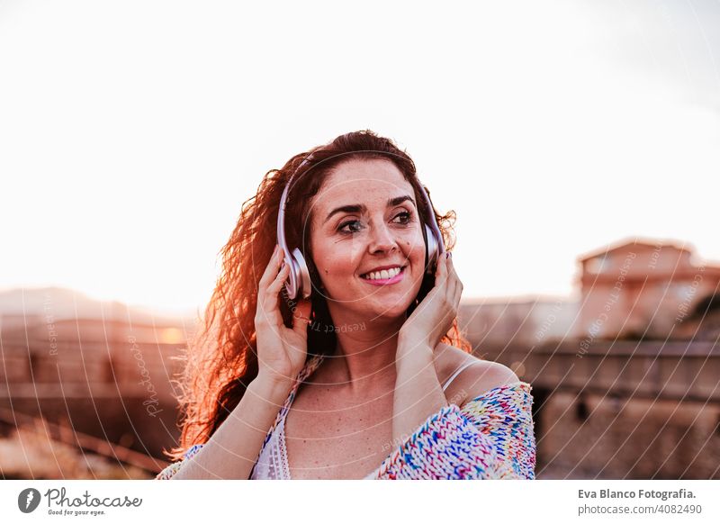 Porträt im Freien von einer jungen schönen Frau bei Sonnenuntergang Musik hören auf Kopfhörer und lächelnd. Lifestyle und Musik Konzept lässig Spaß