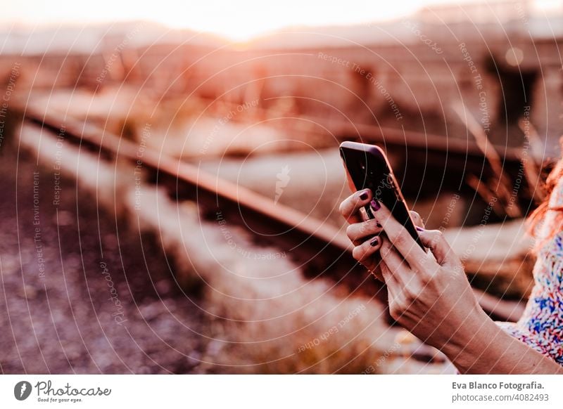 unerkennbare Frau bei Sonnenuntergang mit Handy. Lifestyle und Technologie Konzept lässig Spaß junger Erwachsener App Musik hören warm Textfreiraum Park