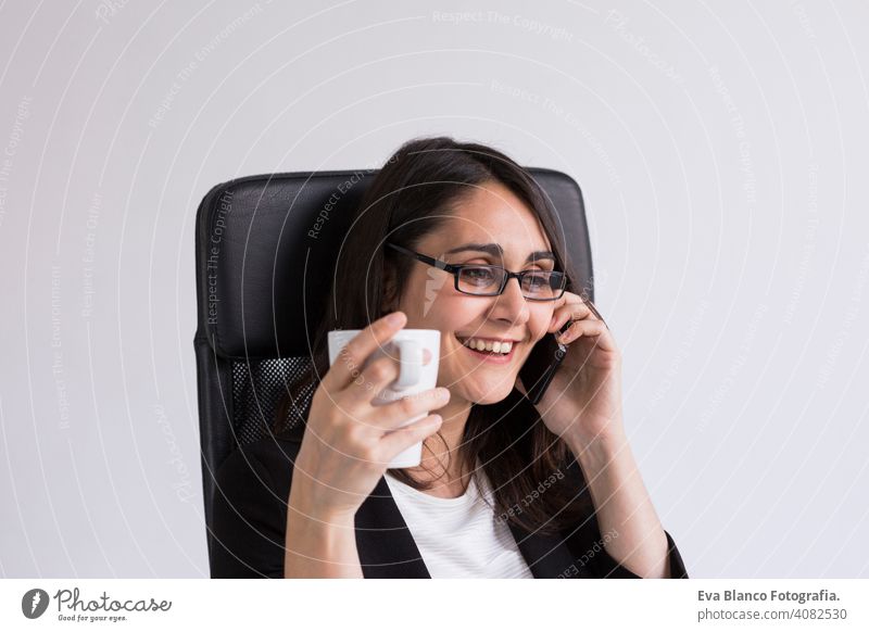 schöne junge Business-Frau spricht auf ihrem Handy im Büro und hält eine Tasse Kaffee. Business-Konzept. Lebensstil. Innenbereich Computer Laptop Arbeiter