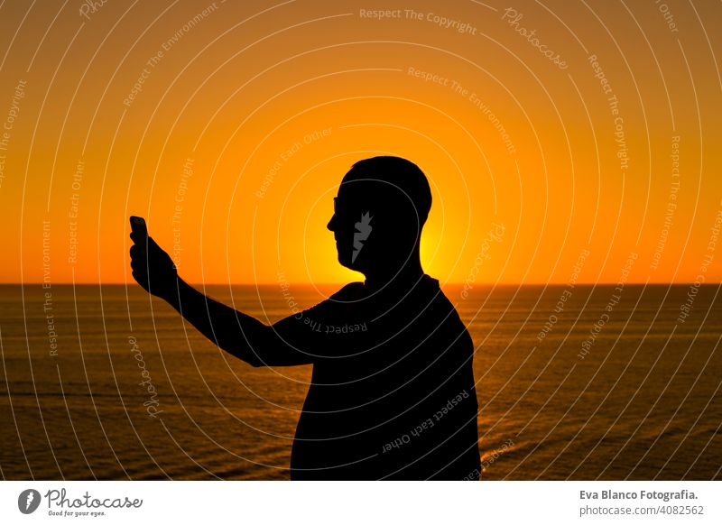 Silhouette eines jungen Mannes mit Mobiltelefon bei Sonnenuntergang. Ozean Hintergrund. Urlaub und Technologie-Konzept Hand Zelle Telefon Person Tourist