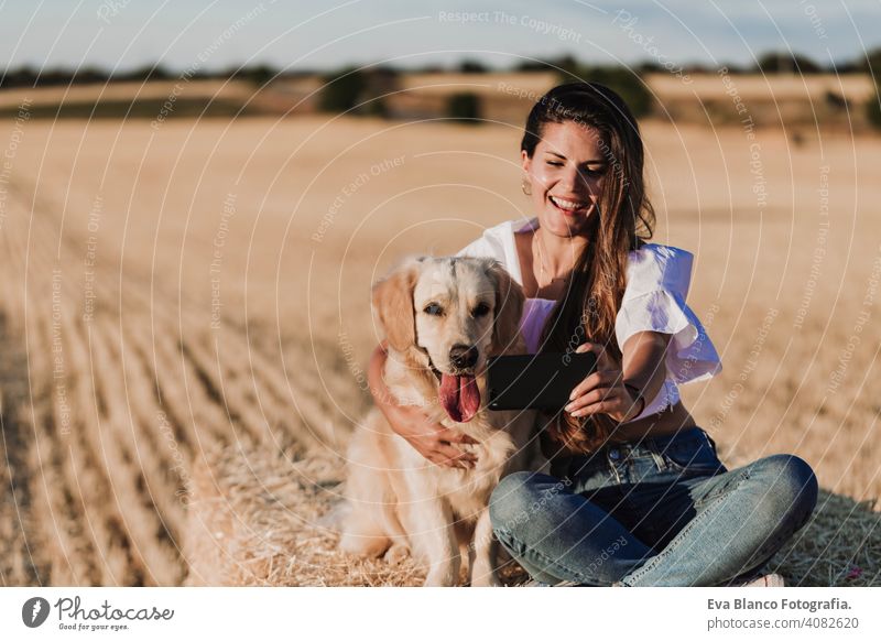 Junge schöne Frau, die mit ihrem Golden Retriever Hund auf einem gelben Feld bei Sonnenuntergang spazieren geht. Natur und Lebensstil im Freien Sommer Mode jung