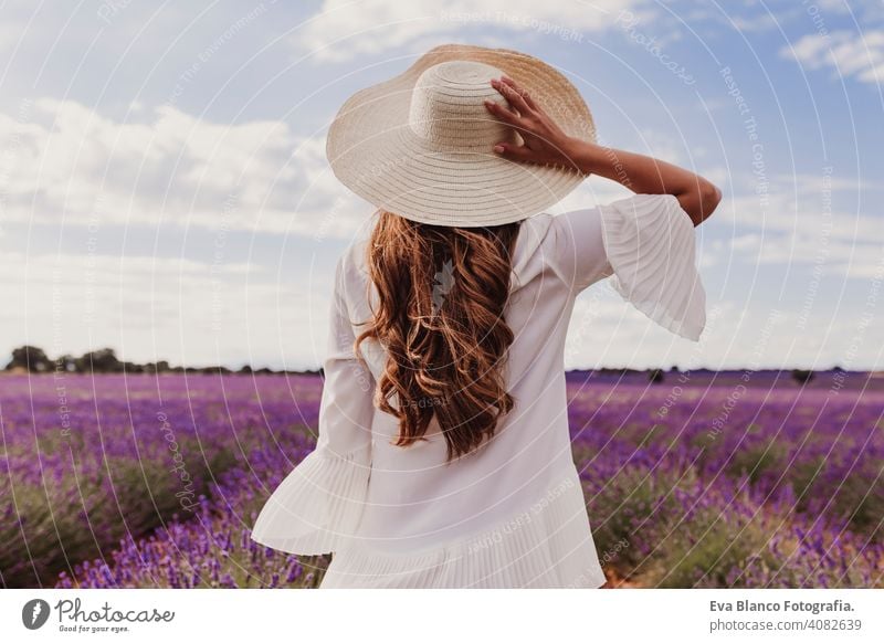 charmante Junge Frau mit einem Hut und weißem Kleid in einem lila Lavendelfeld bei Sonnenuntergang. LIfestyle im Freien. Rückansicht Wiese Schönheit Freude