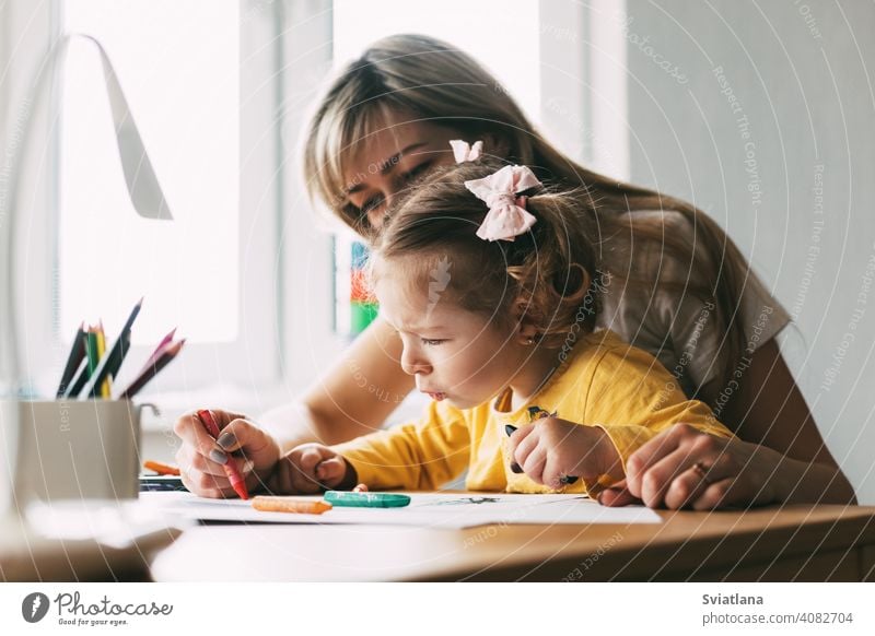 Eine junge Mutter bringt ihrer kleinen Tochter bei, mit Buntstiften zu zeichnen. Gemeinsame Zeit, Kreativität, Bildung. Seitenansicht Mädchen Kind Mama