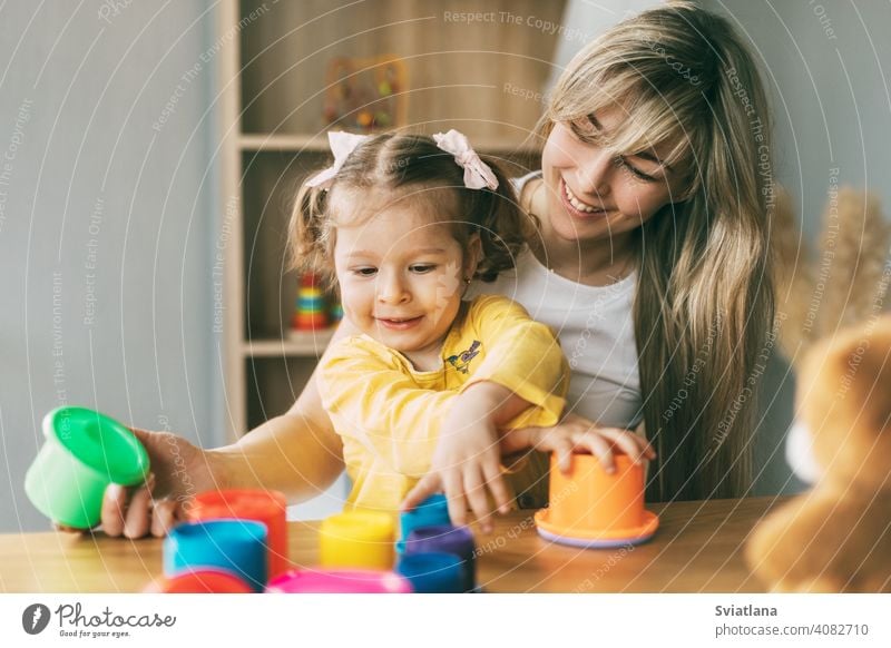 Mama und ein lachendes kleines Mädchen spielen mit bunten Förmchen am Tisch zu Hause. Gemeinsame Zeit, Mutterschaft, Elternschaft Kind heimwärts Spiel Formen