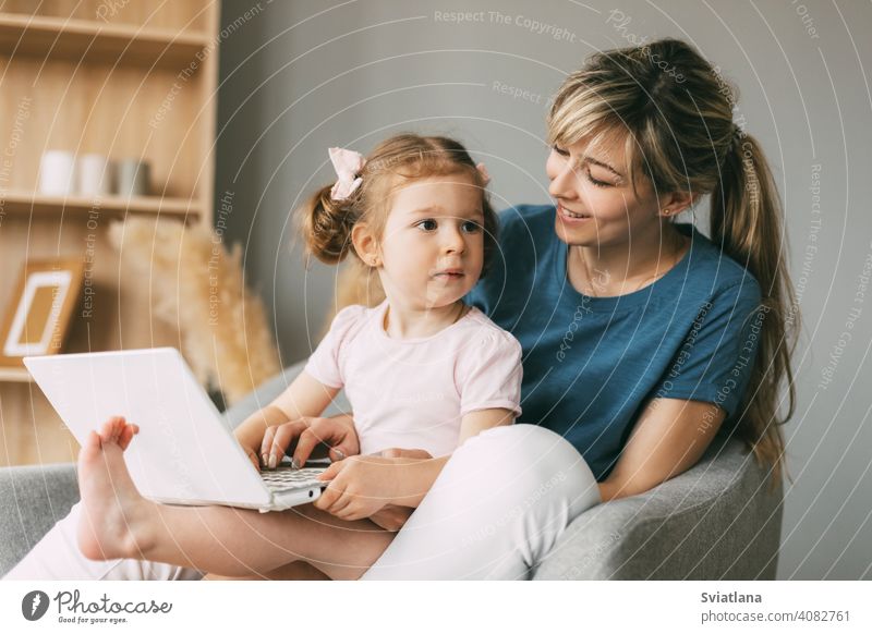 Ein kleines Mädchen und ihre Mutter beobachten Cartoons auf einem Laptop, während sie zusammen auf einem Stuhl sitzen Kind Mama Computer Karikatur online