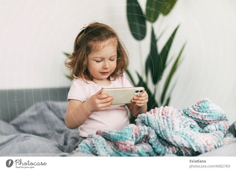 Ein kleines Mädchen sieht sich vor dem Schlafengehen Zeichentrickfilme auf ihrem Telefon an oder spielt auf dem Bett Smartphone Kind Mobile heimwärts Mitteilung