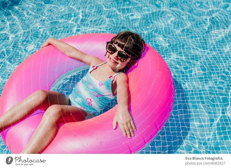 schönes Kind Mädchen schwimmt auf rosa Donuts in einem Pool. Tragen Sie eine Sonnenbrille und lächelnd. Spaß und Sommer Lebensstil Aktivität Schönheit im Freien