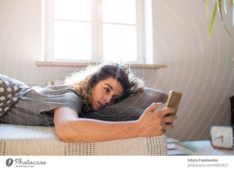 Junge Frau benutzt Smartphone im Bett Morgen Uhr aussruhen Erholung schlafen wach Wecker schläfrig Aufwachen Appartement Freizeit Schlafzimmer Haus heimwärts